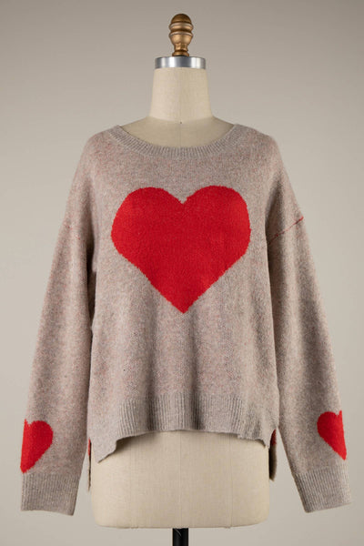 A cozy Cara Heart Cropped Sweater in beige flaunts a bold red heart on the chest with smaller hearts along the sleeves. Displayed on a mannequin against a plain backdrop, it radiates warmth and style.