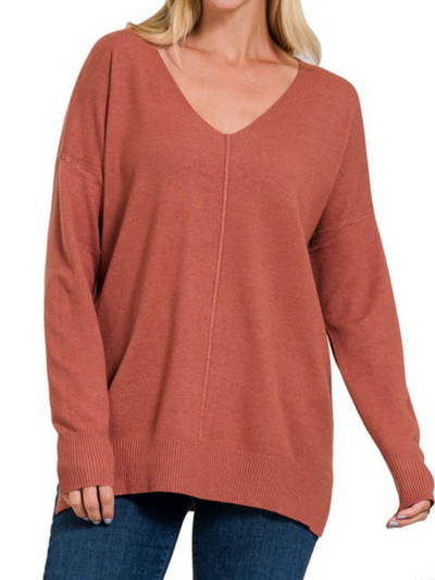 A person is dressed in the Ashley Front Seam Sweater in Heather Rust, a relaxed fit V-neck with long sleeves and a ribbed hem, paired with blue jeans. This sweater exudes luxurious comfort.