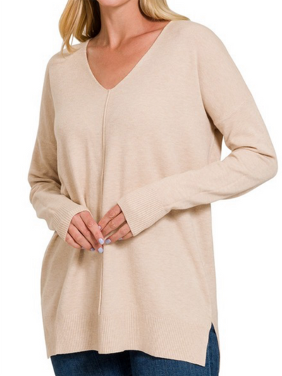 A woman is elegantly showcasing the Ashley Front Seam Sweater in Heather Beige, a fashion piece exuding luxurious comfort. This V-neck sweater with long sleeves is paired beautifully with dark blue jeans against a simple white background, embodying effortless style.