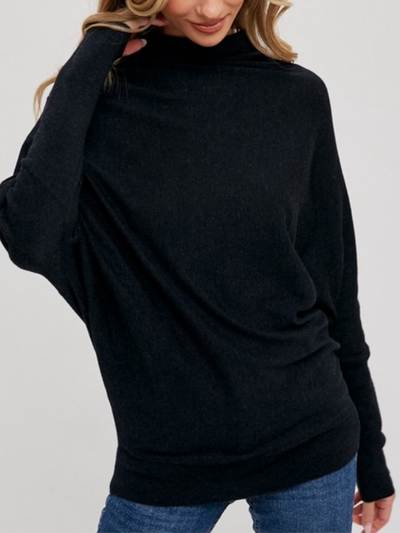 A person in an Ellen Slouch Neck Pullover - Black and blue jeans poses with their hand touching their hair against a plain background.