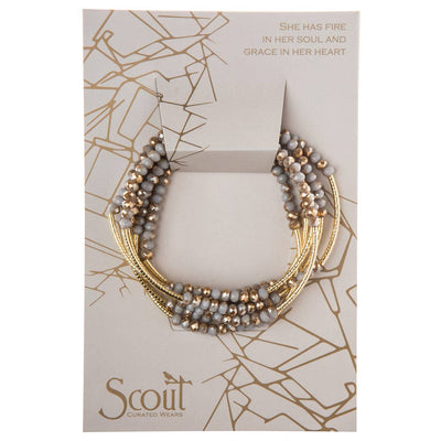 A Scout Wrap - Silver Lining / Gold set of beaded bracelets featuring crystal beads with gray and gold accents is displayed on a card. This versatile accessory showcases the quote, "She has fire in her soul and grace in her heart," making it perfect for layering or wearing solo.