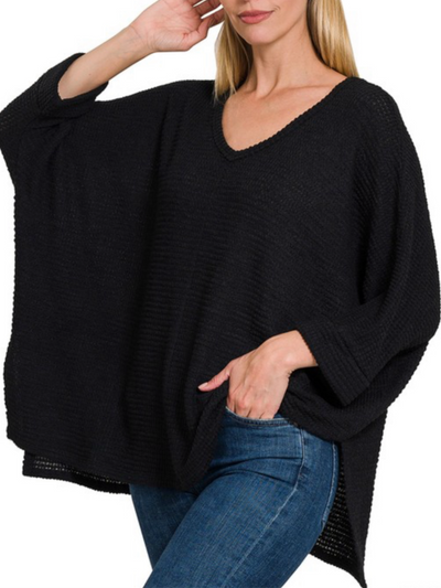 A person wearing the Maddie 3/4 Sleeve Sweater in black and blue jeans stands with one hand on their hip and the other near their head, showcasing a casual pose. The sweater is designed with jacquard fabric, featuring a V-neck style and long sleeves.