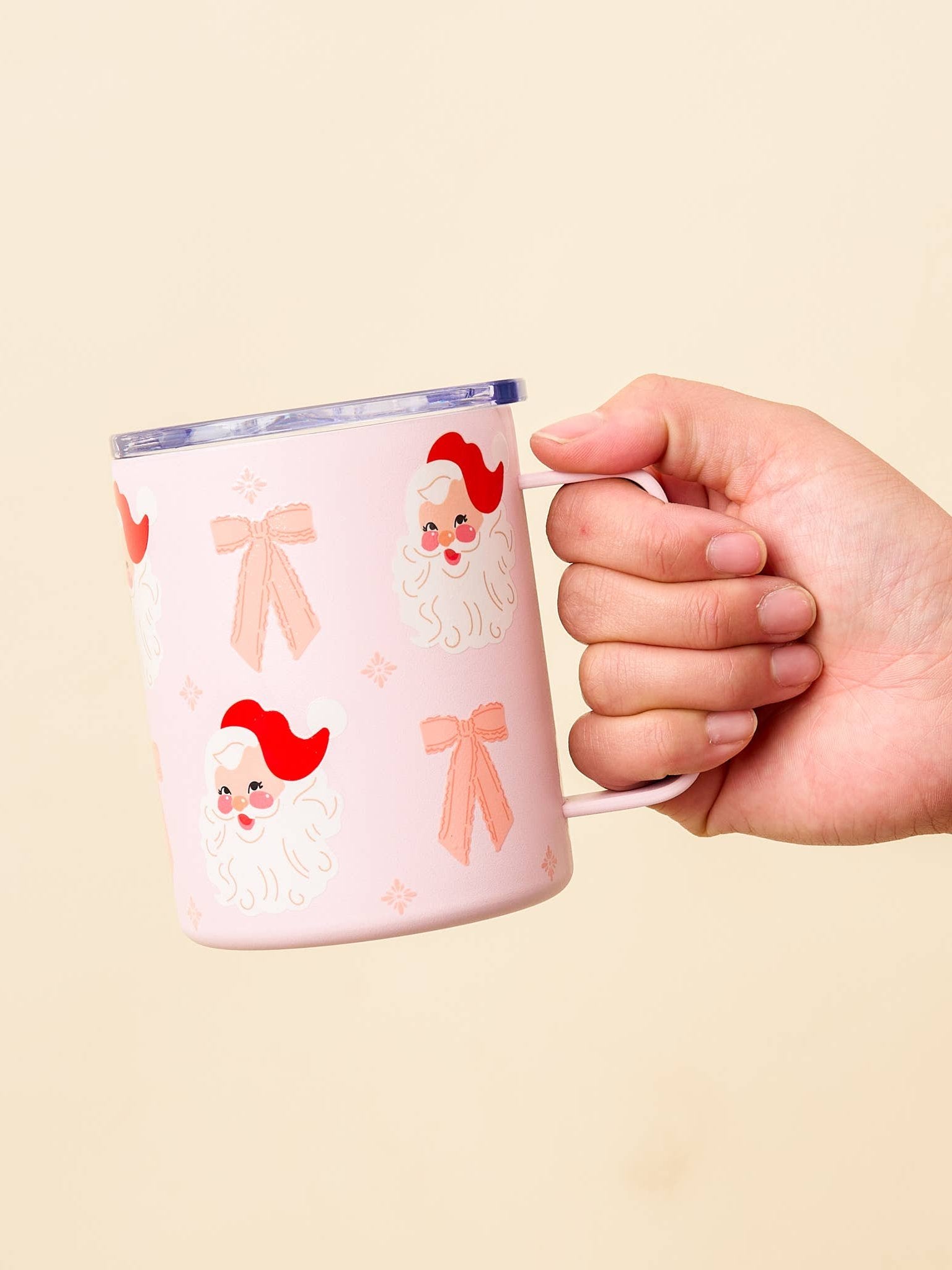 Coquette style pink mug with Santa faces and pink bow designs, held in hand. The perfect holiday accessory for a charming, vintage-inspired look.