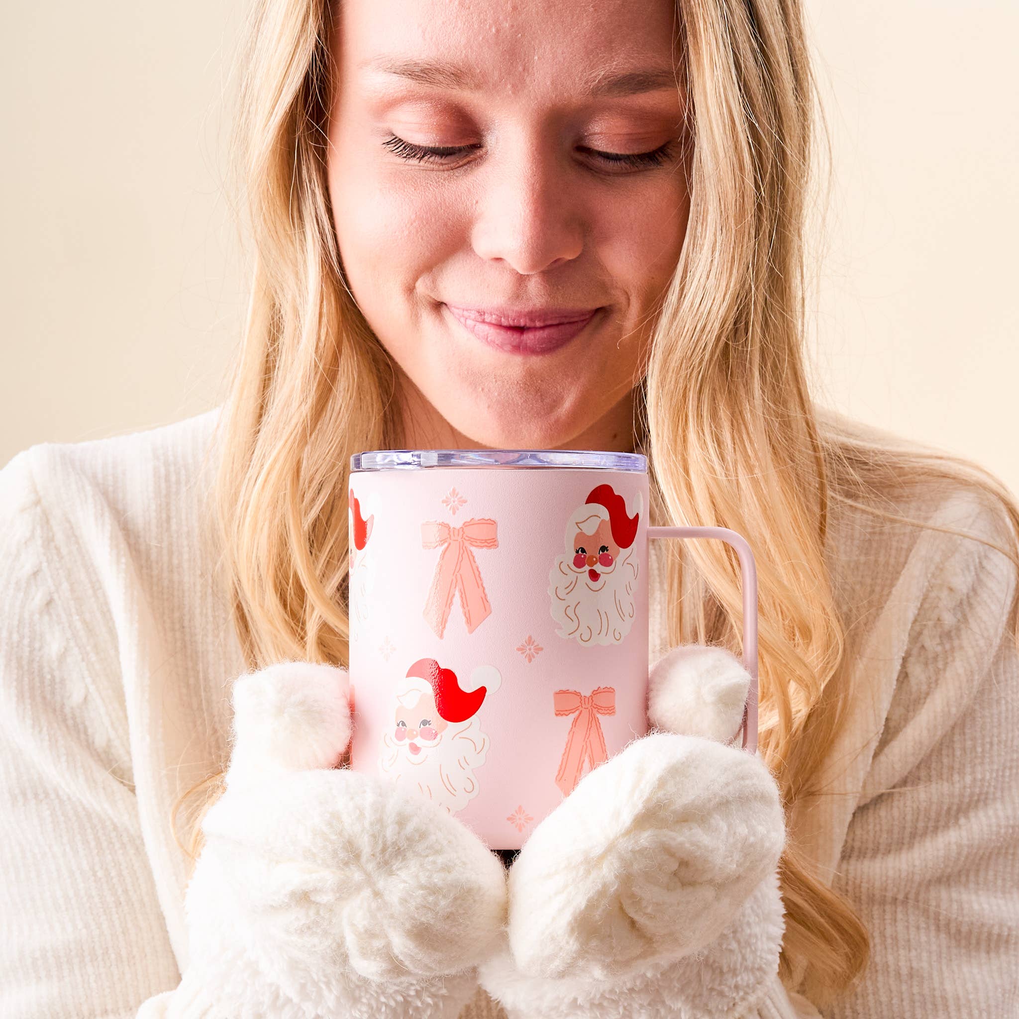 Smiling woman holding a pink Santa mug with a coquette-style design featuring pink bows and retro Santa faces. Cozy and cute for holiday sipping.