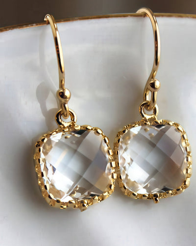 A pair of dainty gold-plated earrings featuring 9mm crystal-clear glass square blocks with a 3mm thickness, hanging from 14k gold-filled earwires, displayed on a white ceramic dish. Perfect for special occasions or everyday elegance.