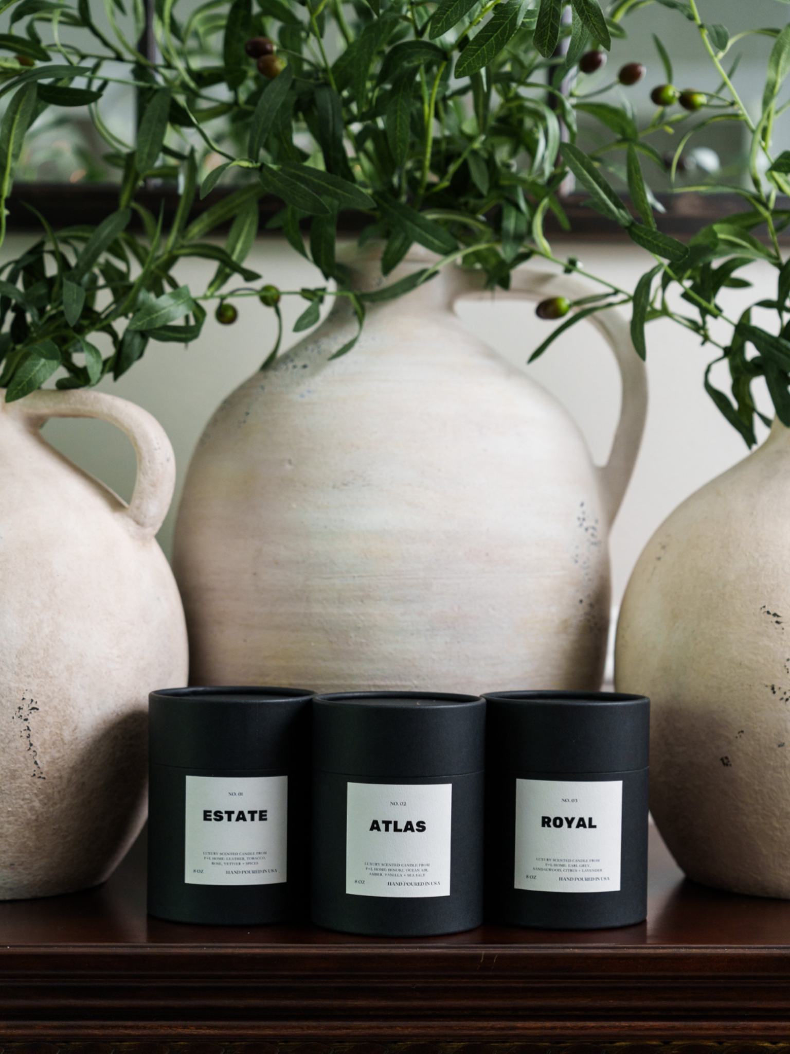 The No. 02 Atlas 8oz Soy Luxury Candle from F+L Home sits gracefully on a wooden surface alongside two other black cylindrical containers labeled 