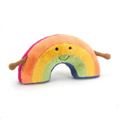 Jellycat Amuseables Rainbow plush toy laid flat, showing its curved rainbow arcs in orange, yellow, and green hues, with small brown arms on each side.