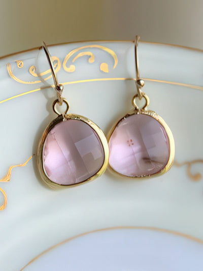 A pair of elegant light pink drop earrings featuring 13mm faceted glass gems set in gold-plated bezels with 14k gold-filled earwires. Displayed on a white ceramic dish with gold detailing, these earrings exude timeless simplicity and grace.