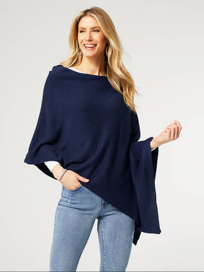 A woman wearing a navy lightweight poncho styled asymmetrically over a white top and blue jeans. The soft, flowing fabric drapes elegantly, showcasing its versatile and relaxed fit. She is smiling confidently, accessorized with silver hoop earrings and a bracelet.