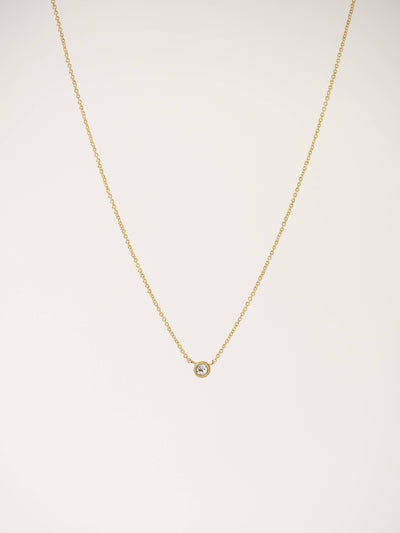 Gold solitaire necklace with a petite Swarovski crystal pendant on a delicate gold chain, displayed against a light neutral background.