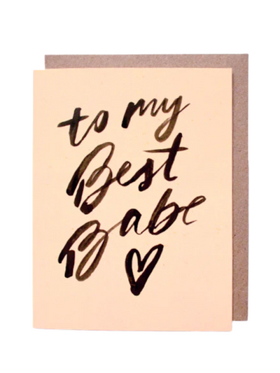 The "To My Best Babe - Card" features black calligraphy with the message on a beige background and a small heart at the bottom. It comes with an eco-friendly brown envelope.