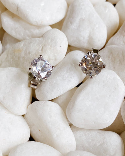 Two Brilliant Cut Sterling Silver Stud Earrings are displayed on smooth white stones.